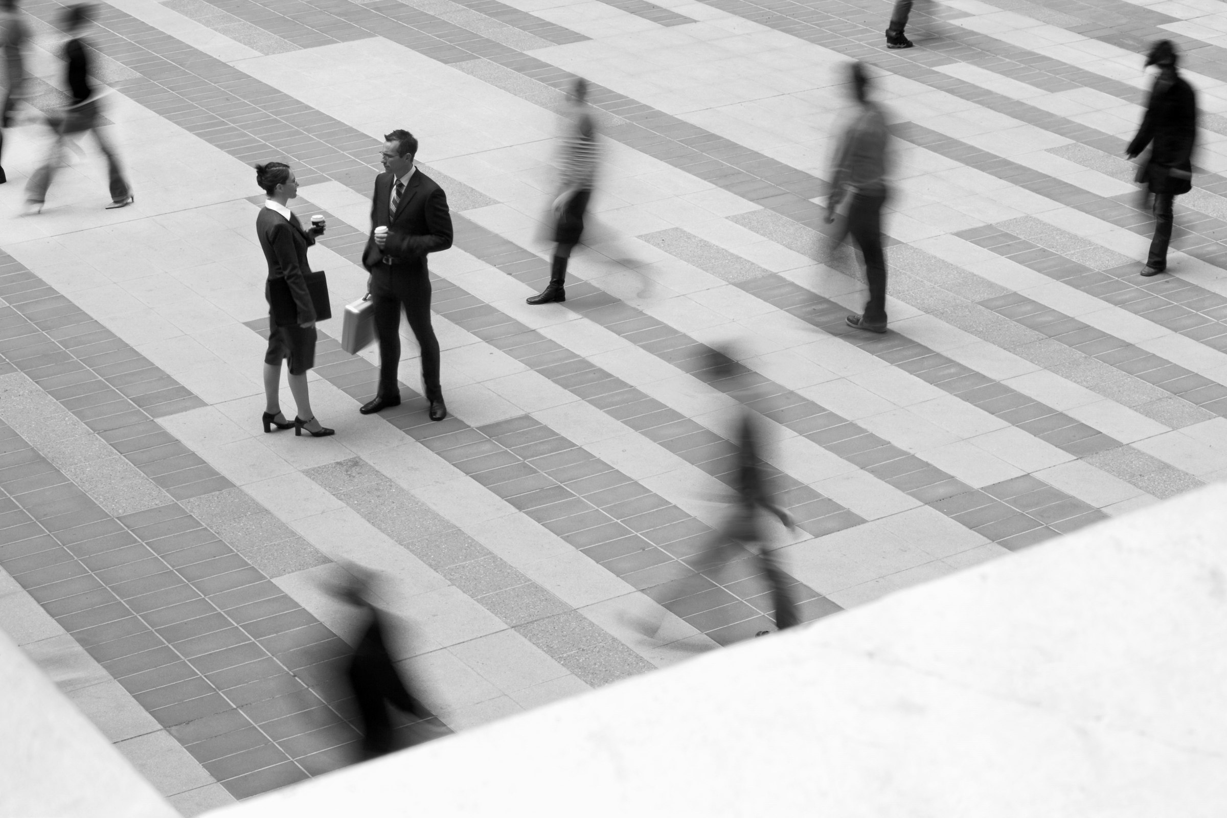 Two people in conversation on a busy city plaza while others move past them